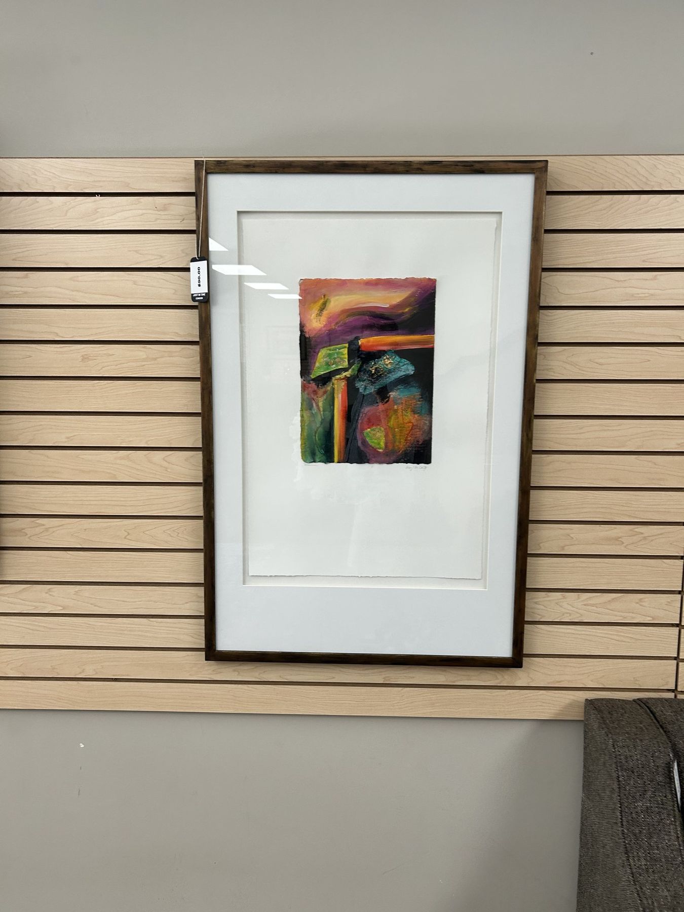 A small framed abstract painting in a wide cream mount on slatwall