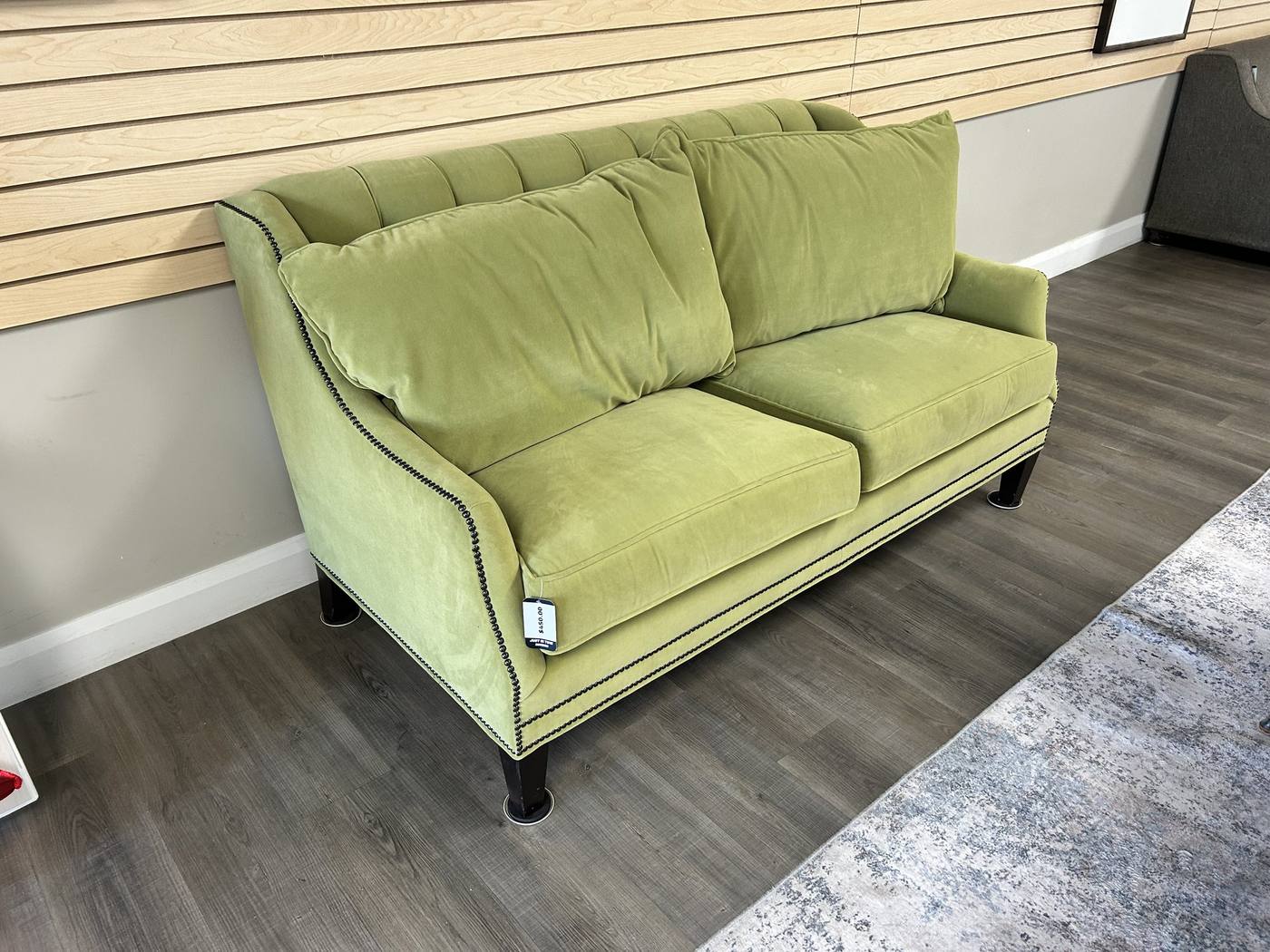 A sage green upholstered loveseat displayed against slatwall in the consignment showroom