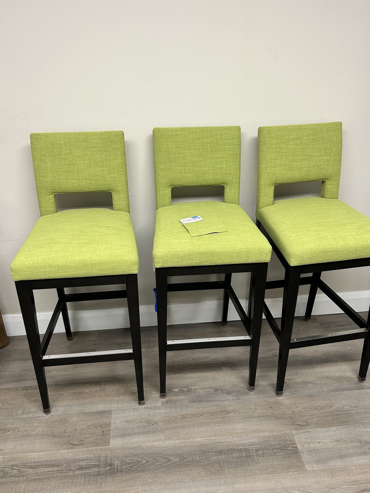 Three lime green upholstered counter stools with dark wood legs on the showroom floor