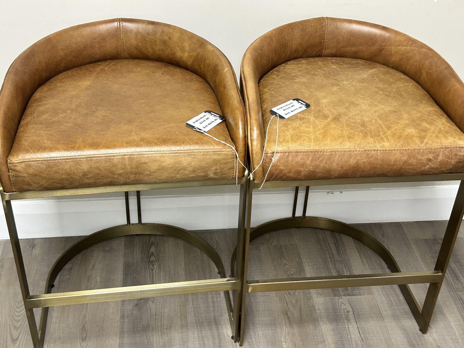 A pair of tan leather barrel-back bar stools with brass bases, tagged and ready to sell