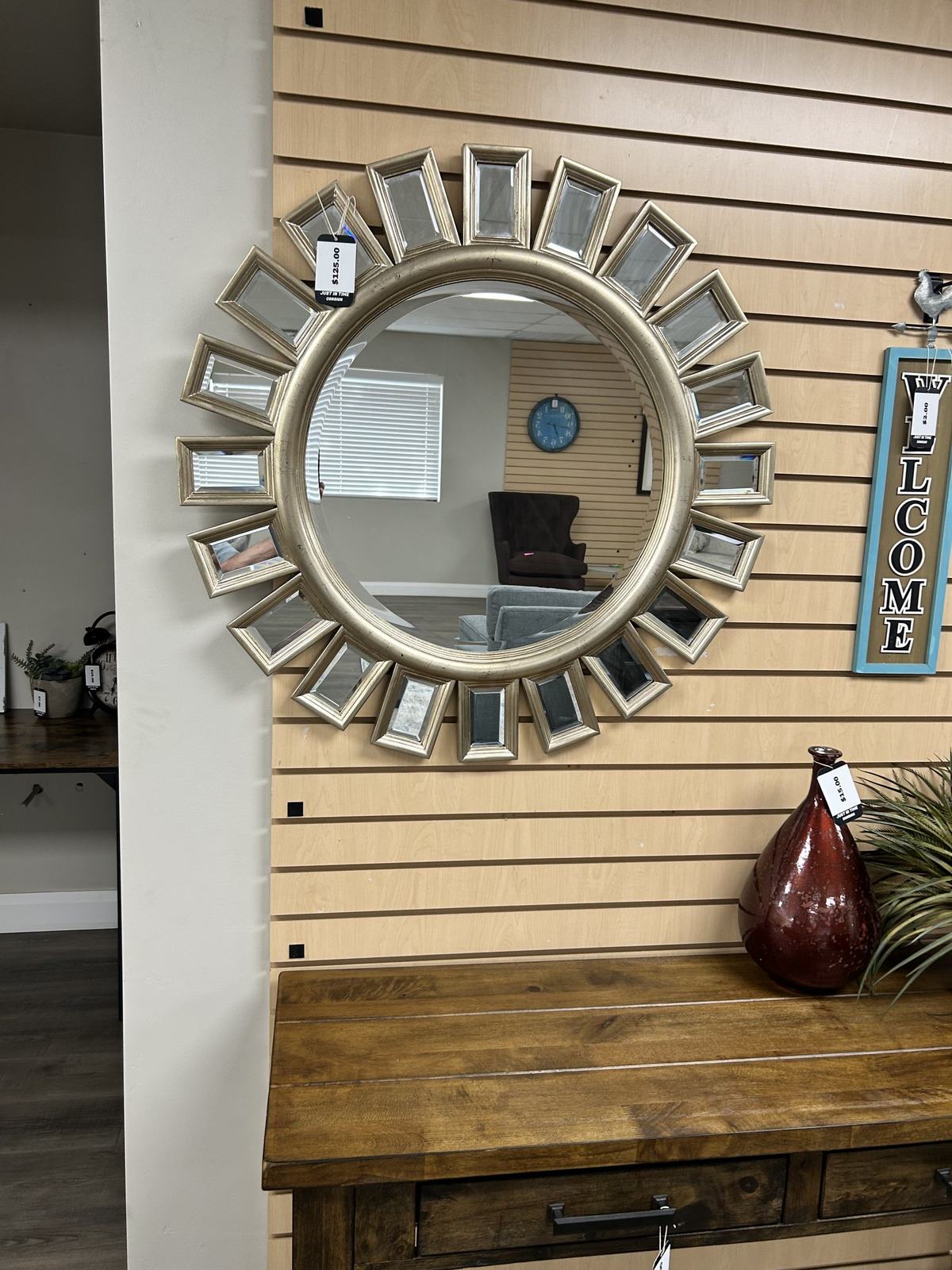 A gold sunburst mirror hung above a rustic wood console table with a decorative vase